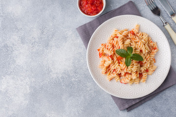 Spiral pasta mixed with cherry tomatoes and tomato sauce on a plate. Copy space