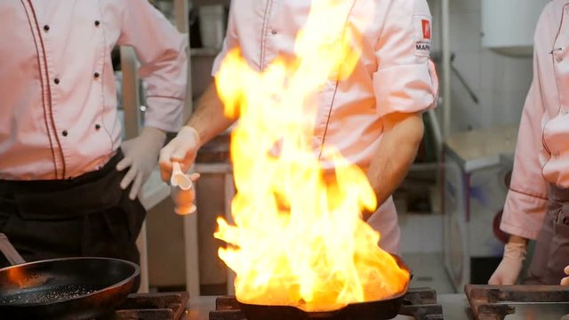 Chefs cooks and doing flambe on beef steak in grill pan in restaurant kitchen
