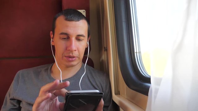 man listening to the music on the train rail car coupe compartment travel. slow motion video lifestyle. man with a smartphone at the window of a train in a car travel internet social media web. man