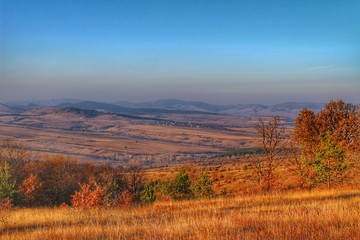 A scenic panoramic view of autumn trees, grass, fields and mountains during sunset at golden hour