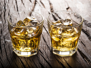 Whiskey glasses or glasses of whiskey with ice cubes on the wooden table.