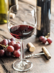 Glass of red wine on the table. Wine bottle and grapes at the background.