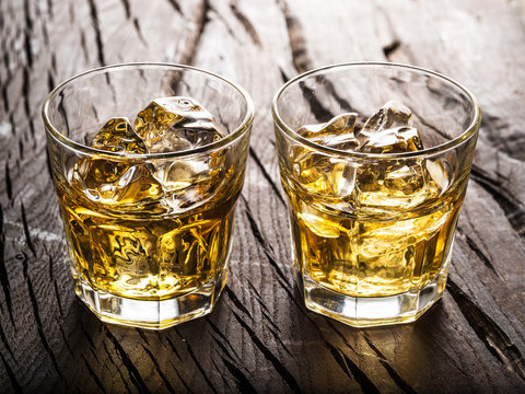 Whiskey glasses or glasses of whiskey with ice cubes on the wooden table.