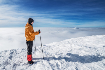 Fototapeta na wymiar Winter hiking. Tourist on snowy mountain top enjoying beautiful view of cloudscape.