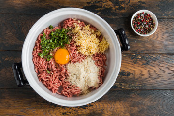 Cooking of meatballs with parmesan. Minced meat, egg, grated cheese, spices, fresh parsley and breadcrumbs in bowl on wooden table. Top view