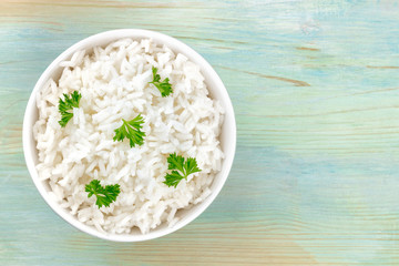 A photo of a bowl of cooked white long rice, shot from the top on a teal blue background with copy...