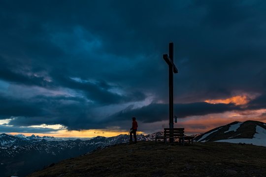 Summit cross Sattele with climber at sunrise, dramatic clouds, Sarntaler Alps, San Martino, Sarntal, South Tyrol, Italy, Europe