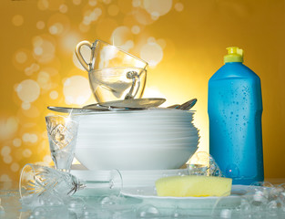 Clean dishes and cups, dishwashing detergent and sponge on yellow background in soap bubbles