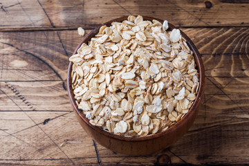 Oatmeal raw in a wooden bowl on a rustic wooden background.