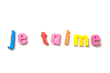 closeup of colorful plastic letters on white background - je t aime in french, traduction of "I love you" in english