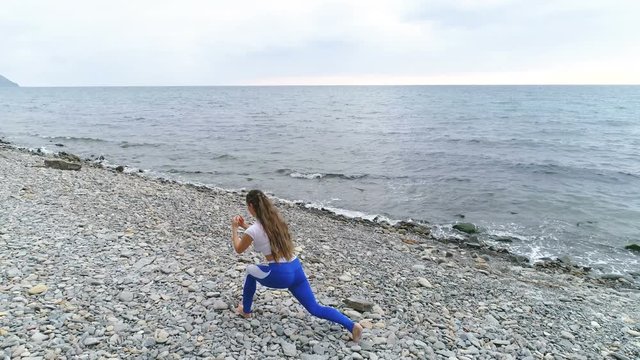 Girl doing squat lunge the bodyflex during breathing exercises on the rock and sea background.