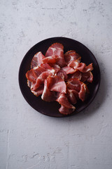 Thin ham slices on wooden plate on white concete background