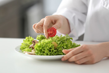 Young female chef preparing tasty salad in kitchen, closeup