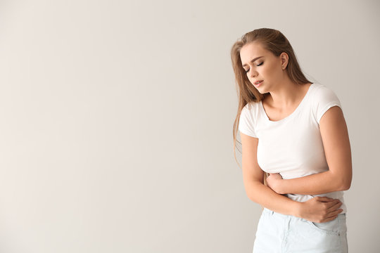 Young woman suffering from abdominal pain on light background