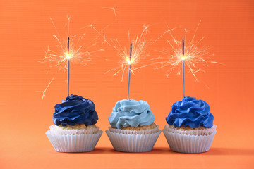 Tasty cupcakes with sparklers on color background