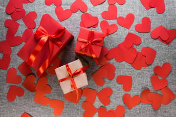 The gift box is wrapped in a red ribbon, and with paper hearts around, on a gray background