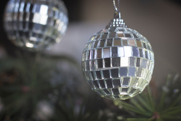 A disco ball like christmas tree toy hanging on a pine tree branch with pine needles.