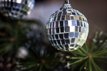 A disco ball like christmas tree toy hanging on a pine tree branch with pine needles.