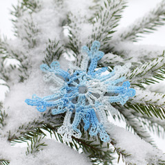magic winter close-up Blue snowflake is connected manually on a snow-covered branch of a Christmas tree