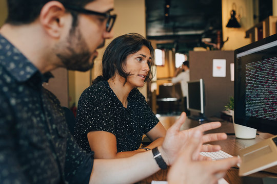 Female computer programmer having discussion with colleague at desk in office