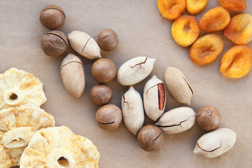 macadamia, Brazil nuts, Bertholletia, pecan dried pineapples and apricots on brown wrapping paper. roasted and notched exotic shell nuts background.