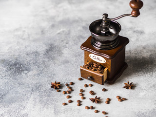 Open wooden manual coffee grinder with scattered coffee grains and anise stars on gray background. Copy space