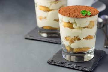 Traditional italian Tiramisu dessert cake in glass, decorated with cocoa powder and mint, on a gray background, horizontal, copy space