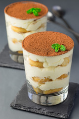 Traditional italian Tiramisu dessert cake in glass, decorated with cocoa powder and mint, on a gray background, vertical