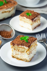 Two piece of traditional italian Tiramisu dessert cake on a white plate, decorated with cocoa powder and mint, on a gray background, vertical