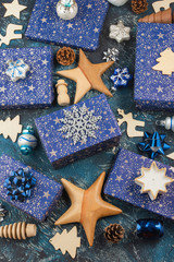 Creative chritmas arrangement. Presents in dark blue wrapping paper with silver stars sparkles, wooden decorations, ornaments, baubles on blue table, top view, selective focus