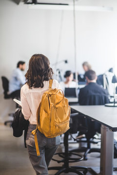 Rear view of businesswoman with backpack walking by desk in creative office