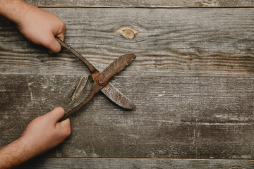 Partial view of worker holding vintage rusty carpentry scissors on wooden background