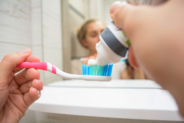 Woman hand holding a toothbrush with a toothpaste applied on it in the bathroom. Close up of female...