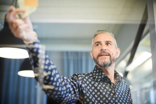 Businessman sticking adhesive note on glass in office