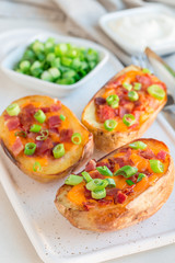 Baked loaded potato skins with cheddar cheese and bacon on ceramic plate, garnished with scallions and sour cream, vertical