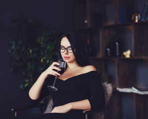 Young celebrating woman black dress. Beautiful model portrait in room hold wine glass.