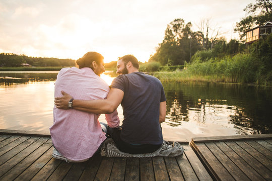 Friends looking at lake while sitting on dock during sunset