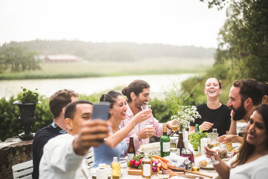 Man taking selfie of friends enjoying dinner at table during party in backyard