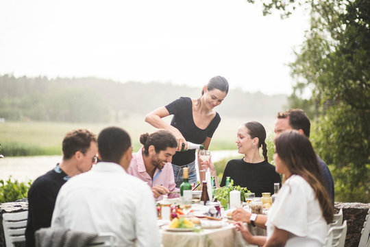 Woman serving drink to female friend during dinner party in backyard