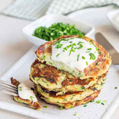 Vegetarian zucchini fritters or pancakes, served with greek yogurt and green onion on ceramic plate, square format