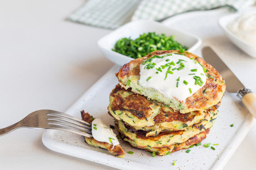 Vegetarian zucchini fritters or pancakes, served with greek yogurt and green onion on a ceramic plate, horizontal, copy space