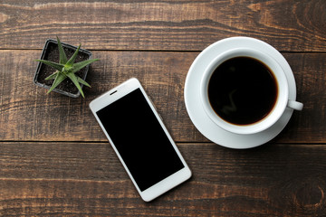 Smartphone white and a cup of coffee on a brown wooden table. view from above