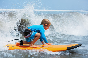 Happy baby boy - young surfer ride on surfboard with fun on sea waves. Active family lifestyle, kids outdoor water sport lessons and swimming activity in surf camp. Beach summer vacation with child.