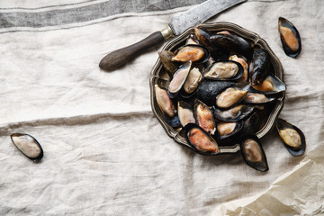 Frozen mussels in metallic vintage plate on linen tablecloth with stripes. Overhead view with text space