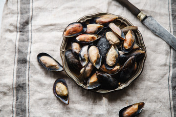 Frozen mussels in metallic vintage plate on linen tablecloth with stripes