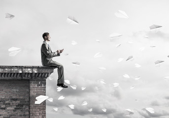 Man on roof edge send message with smartphone and cityscape at b