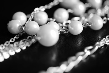 Necklace of white beads and metal chain on a dark background close up. Black and white