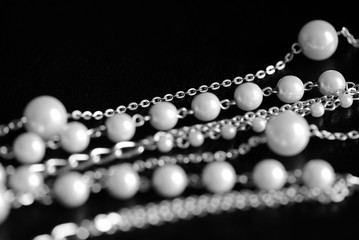 Necklace of white beads and metal chain on a dark background close up. Black and white