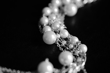 Necklace of white beads and metal chain on a dark background close up. Black and white