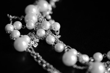 Necklace of white beads and metal chain on a dark background close up. Black and white